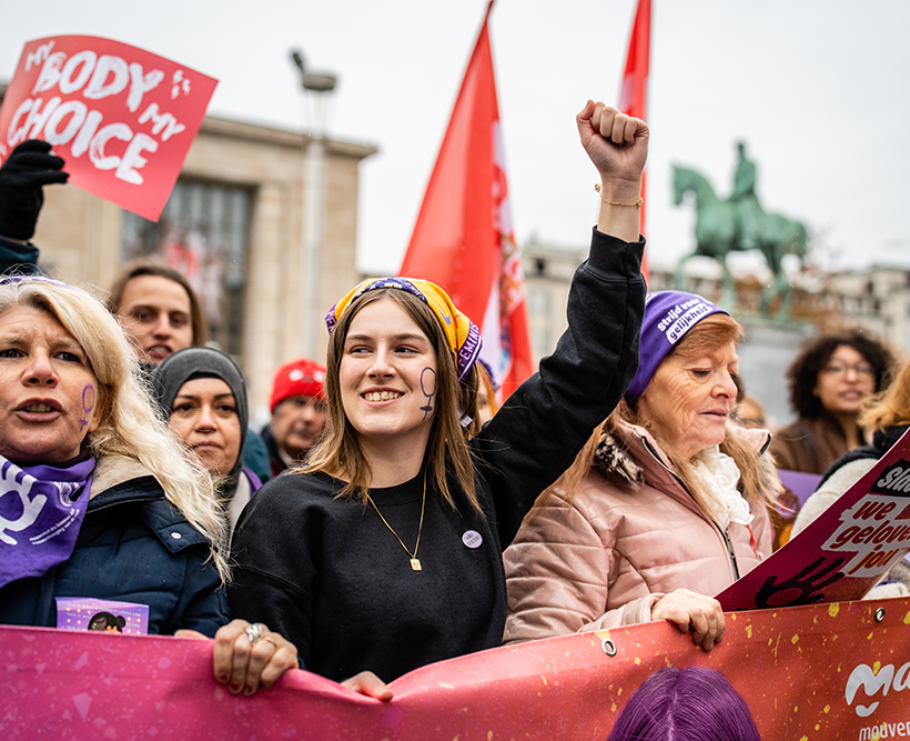 Een jonge vrouw van PVDA-vrouwenbeweging Zelle met de vuist in de lucht tijdens een betoging voor vrouwenrechten