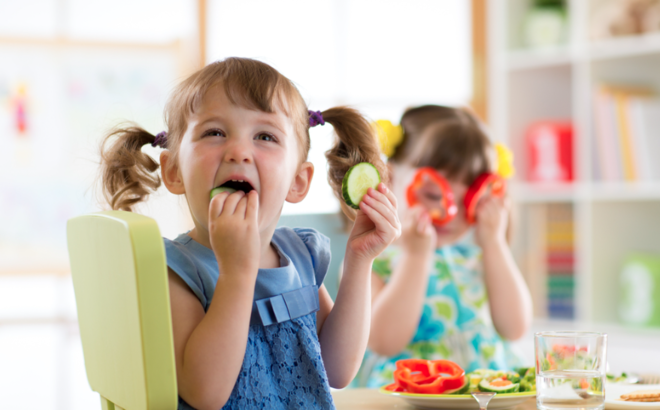 Une petite fille mange des légumes à l'école.