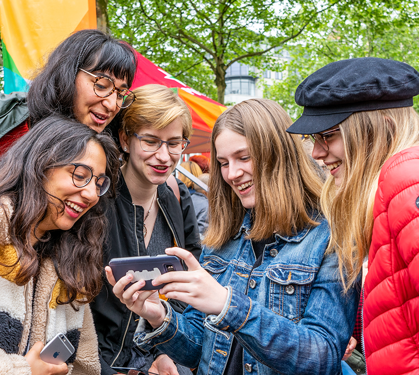 Cinq jeunes personnes regardent un smartphone avec un air enthousiaste.