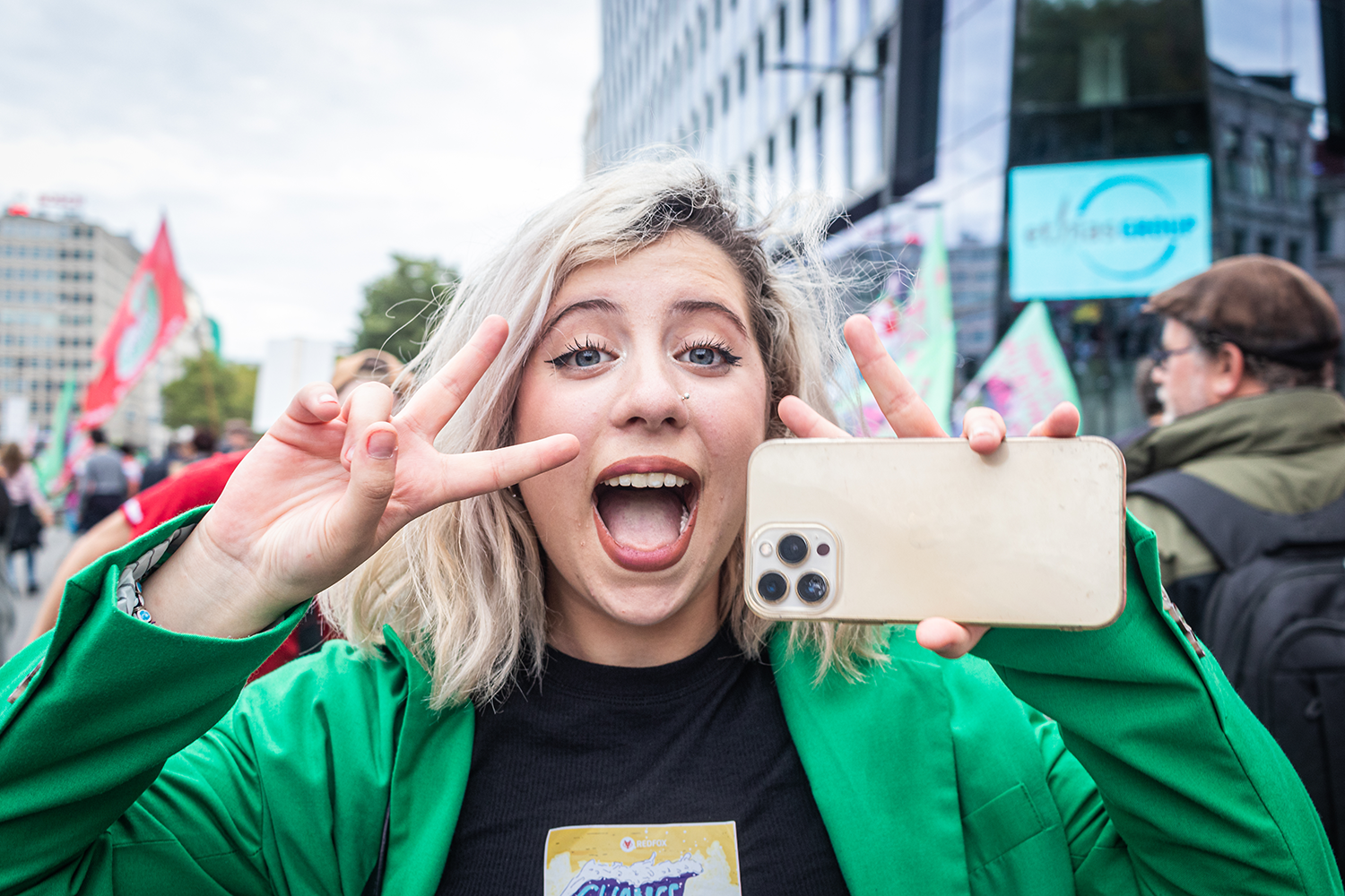 Une jeune femme fait le signe "V" avec sa main tout en tenant un smartphone.