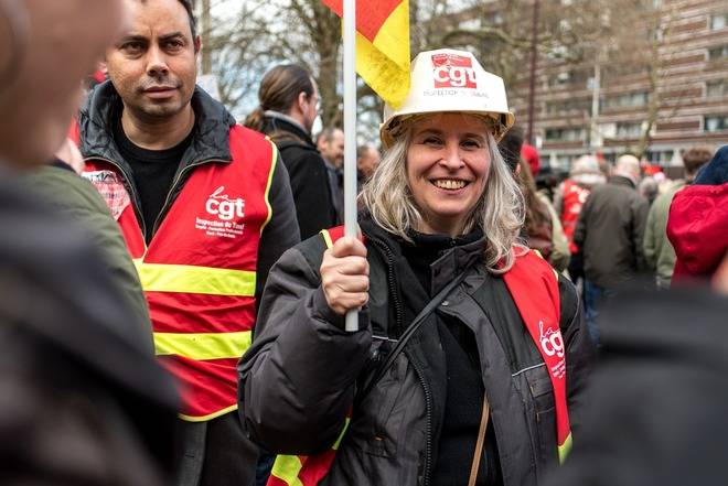 Une femme manifeste avec un casque et une veste portant le logo de la CGT.