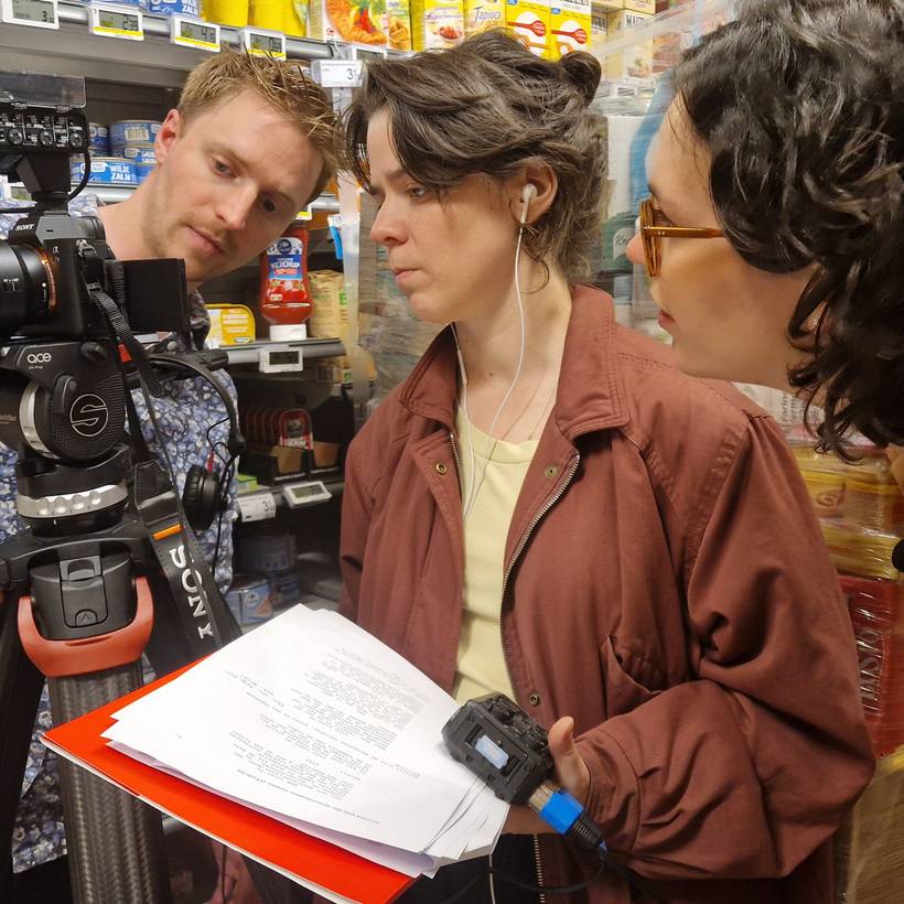 Trois personnes regardent attentivement l'image sur une caméra. Une personne tient un script et un enregistreur audio.