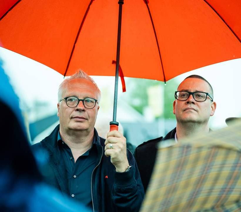 Peter Mertens en Raoul Hedebouw onder een paraplu tijdens een 8 mei-viering