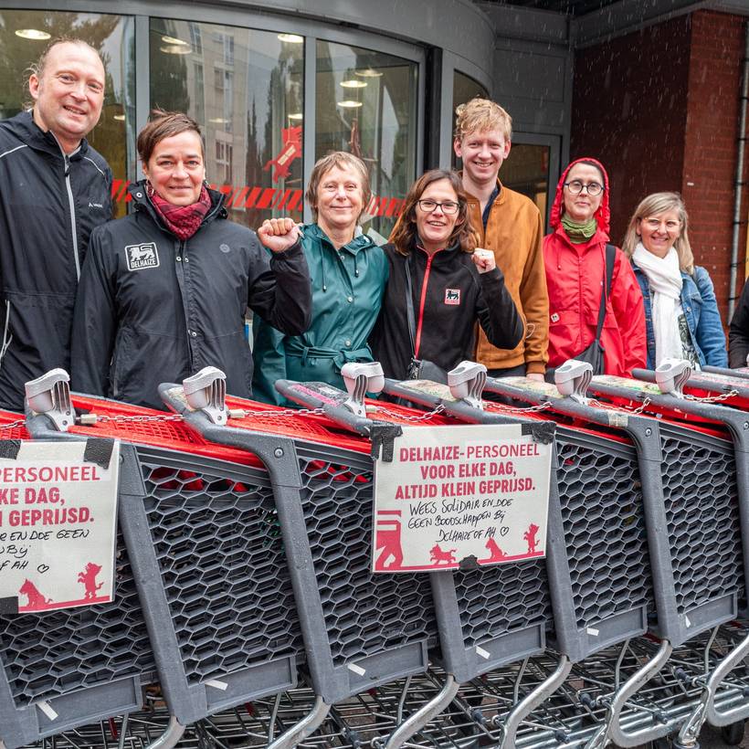 Des membres du PTB posent avec des travailleurs de Delhaize derrière une rangée de caddies où sont placées des pancartes encourageant au boycott. 