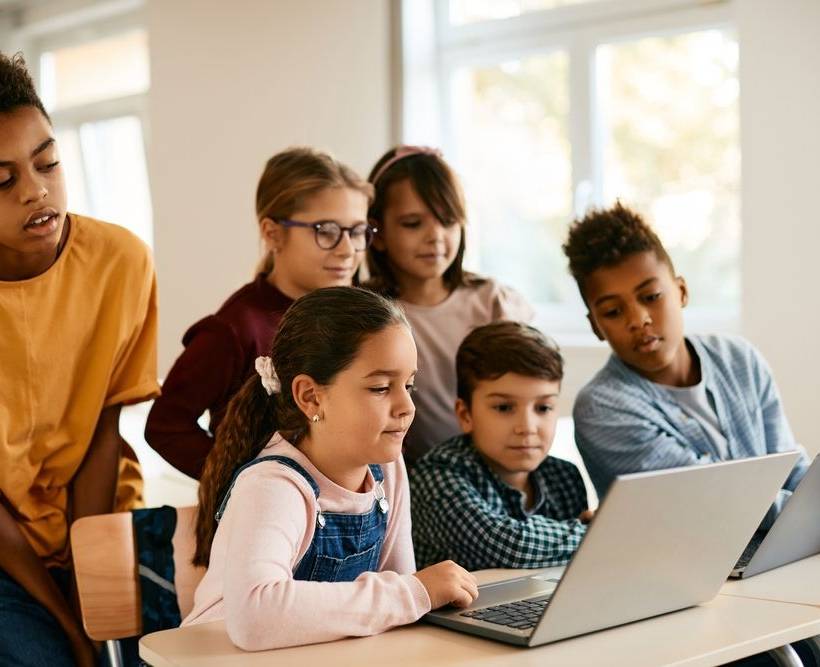 Des enfants regardent ensemble l'écran d'un ordinateur dans une salle de classe.