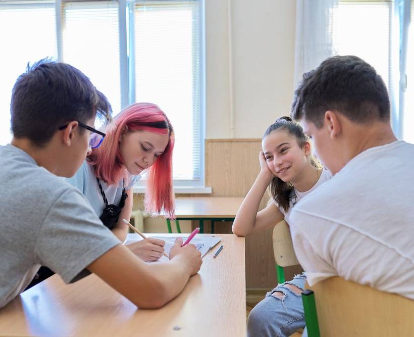 Quatre adolescents dialoguent en groupe autour d'un banc dans une salle de classe.