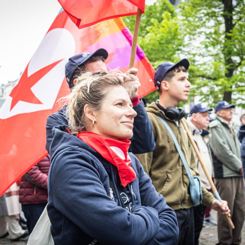 Beeld van een jonge vrouw die een vlag vastheeft met het logo van PVDA op een 1 mei betoging.