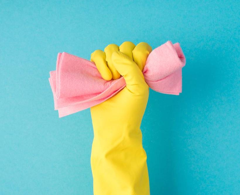 Een hand in een schoonmaakhandschoen houdt een spons in de vuist gekneld