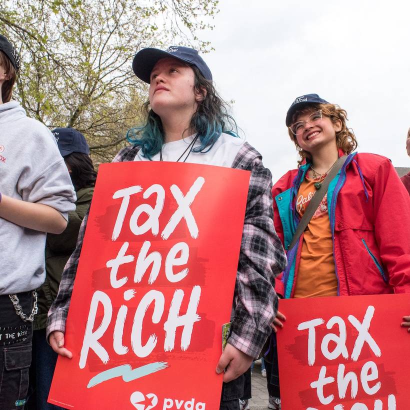 Jonge mensen met een bord 'Tax the rich' op een 1 mei-actie van de PVDA