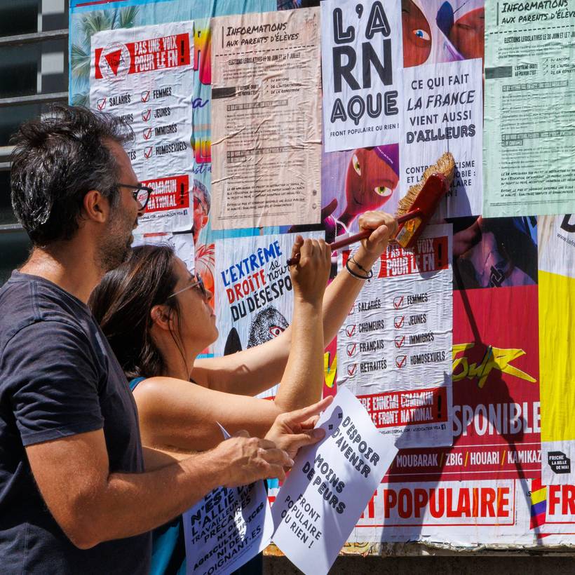 Twee personen plakken verkiezingsaffiches op aanplakborden in Frankrijk