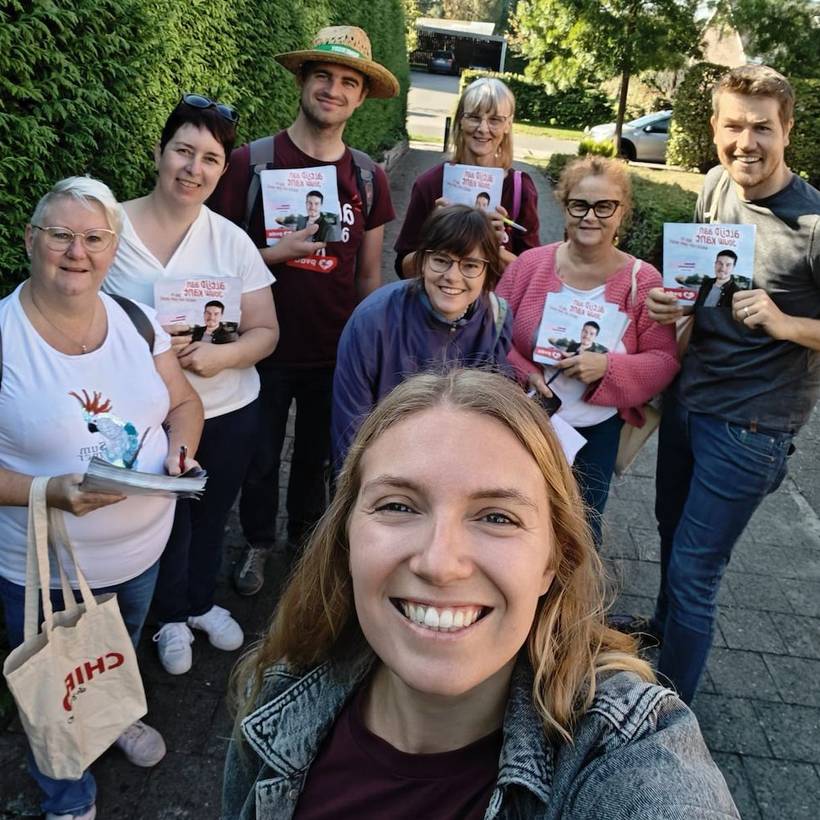 Un selfie pris par une membre du PTB, avec une jeune femme au premier plan et un groupe de membres du PTB souriants derrière elle.