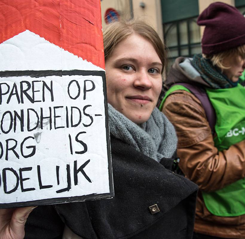 vrouw houdt een groot sigarettenpakje vast met de slogan 'besparen op gezondheidszorg is dodelijk'