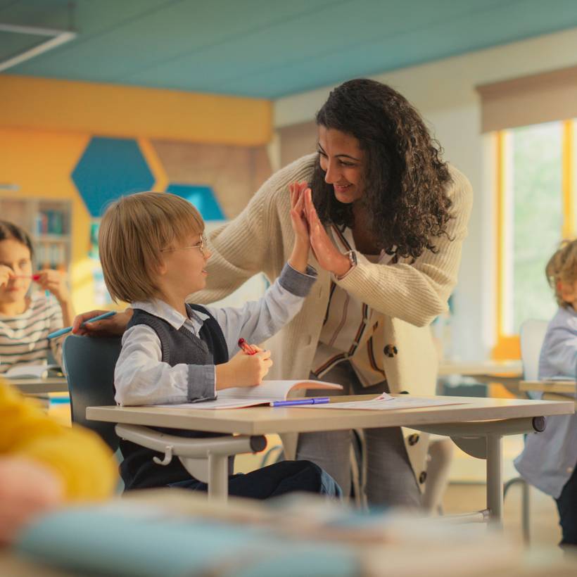 Une enseignante fait un "check" de la main avec un enfant dans une salle de classe