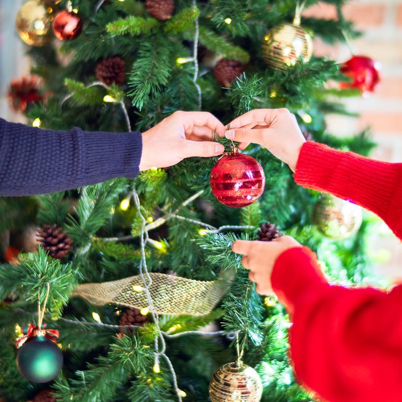 Deux personnes accrochent une boule décorative au sapin.