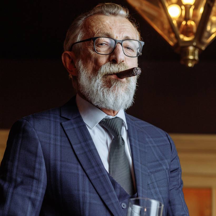 Een miljonair met een sigaar en een glas alcohol kijkt neer op de camera.