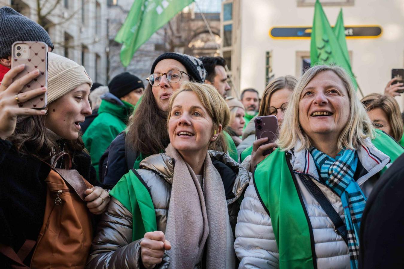 Drie vrouwen met groene hesjes kijken hoopvol naar het podium van PVDA