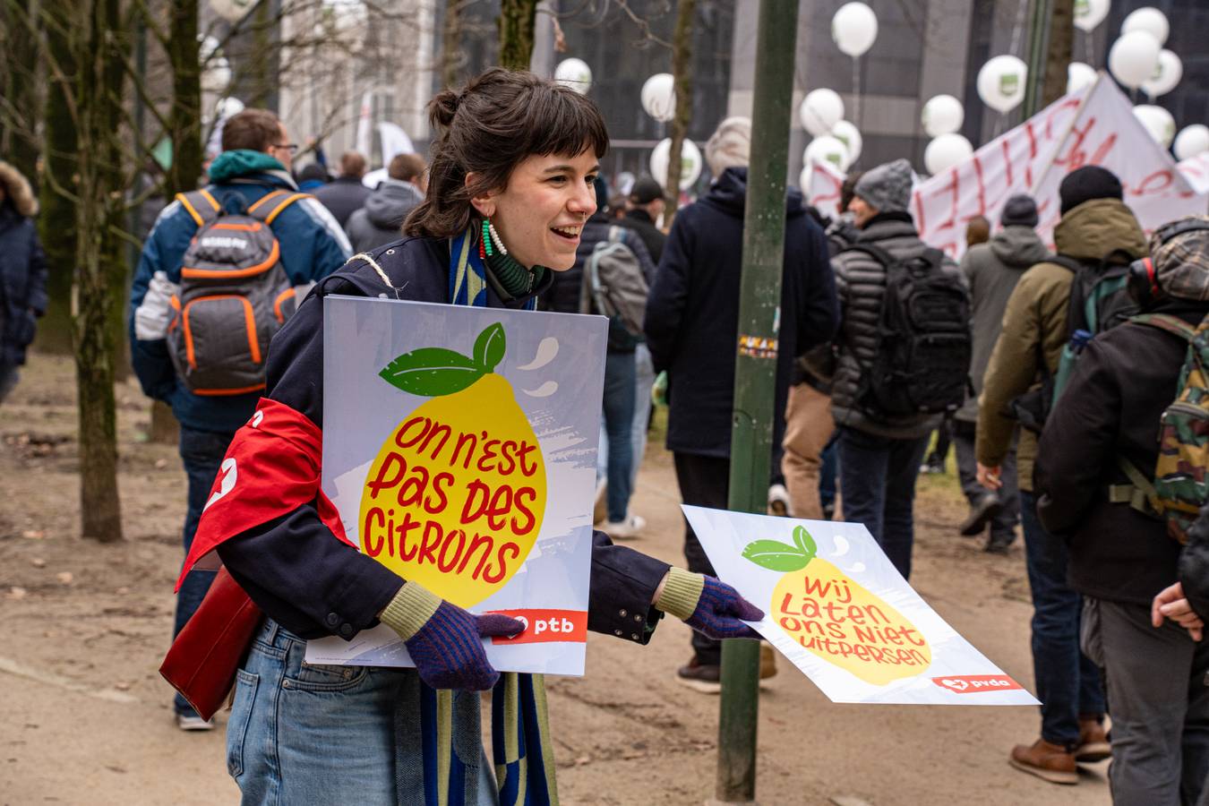 vakbondsbetoging 13 februari: jonge vrouw deelt pancartes uit "Wij laten ons niet uitpersen"