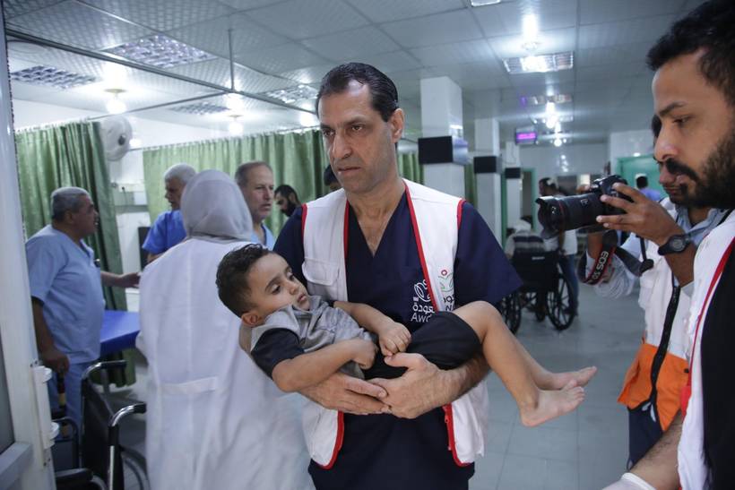 Dr. Ahmad Muhanna, directeur van het Al Awda ziekenhuis in Jabalia, draagt een gewond kind weg