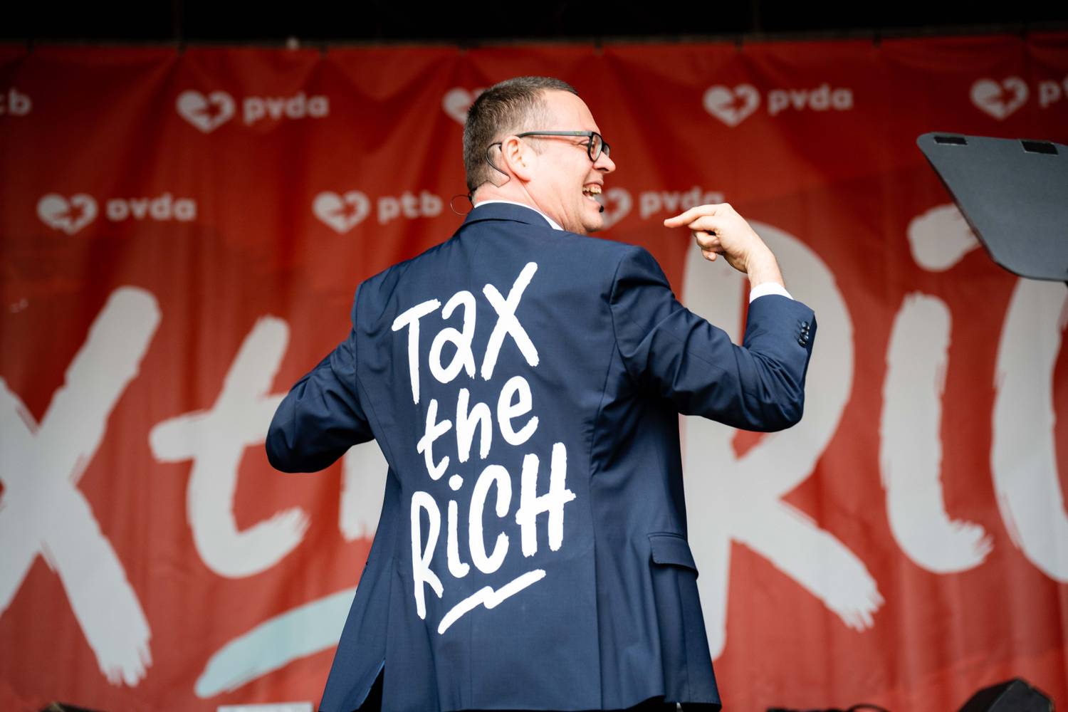 Raoul Hedebouw toont tijdens zijn toespraak zijn vest waar 'tax the rich' op geschreven staat 