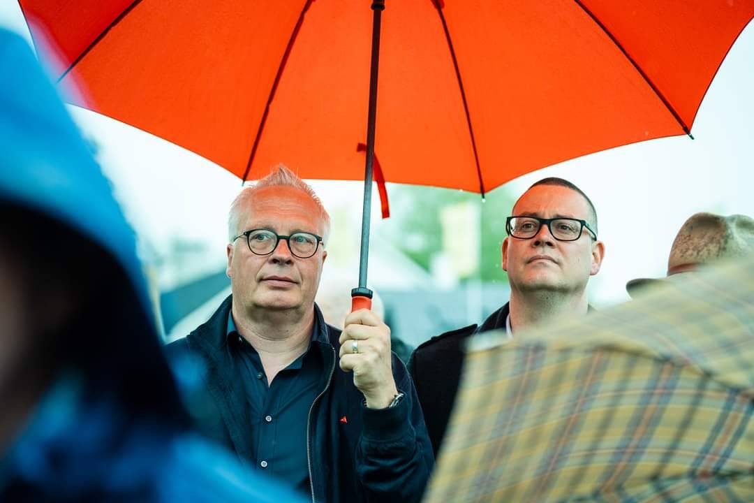 Peter Mertens en Raoul Hedebouw onder een paraplu tijdens een 8 mei-viering