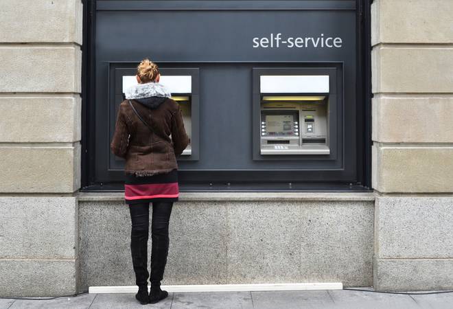 Une femme se tient debout de dos devant un distributeur de billet.